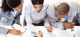 3 IT Consultants working at a desk with a laptop and paperwork